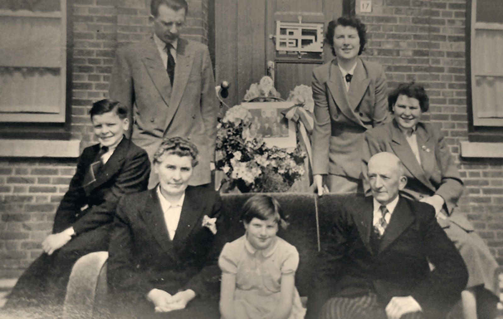 The Van Overveld family posed outside the front door of a brick house, three standing at the back and four seated in front