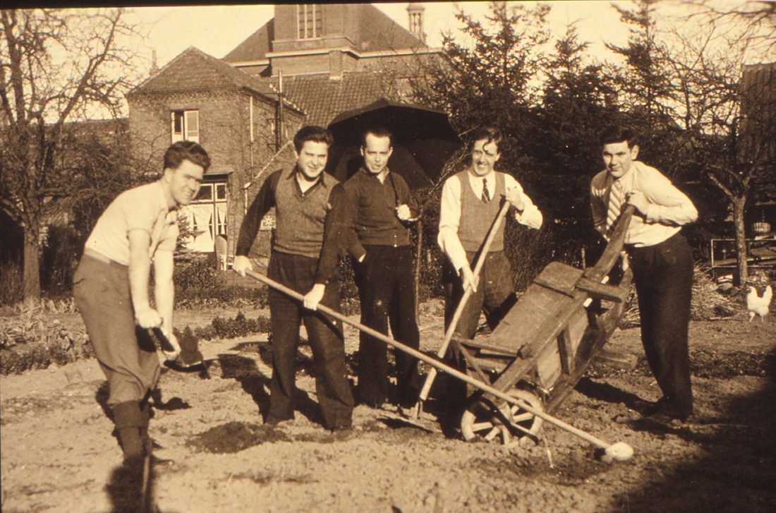 Jonge mannen aan het werk in een tuin met spades en een kruiwagen